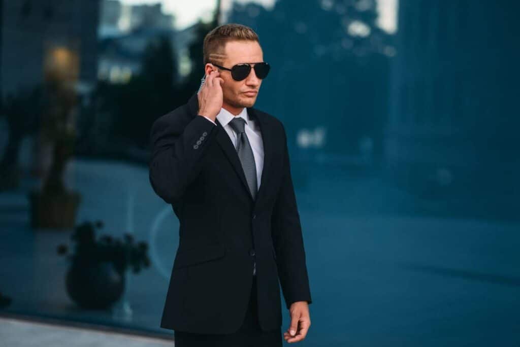 A man in a suit and sunglasses is engaged in a phone conversation while standing outdoors.